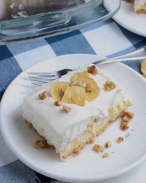 Delicious banana pineapple dessert cut and placed on a white plate. This dessert is garnished with banana slices and small bits of walnut pieces.