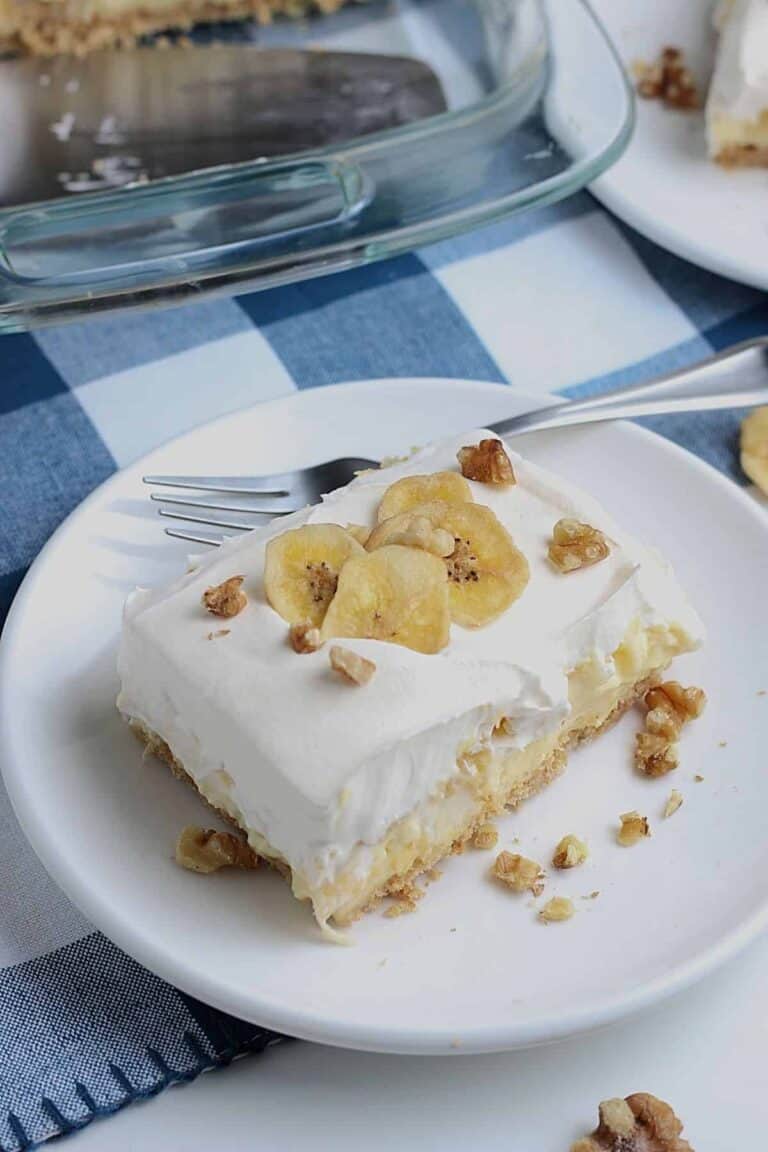 Delicious banana pineapple dessert cut and placed on a white plate. This dessert is garnished with banana slices and small bits of walnut pieces.
