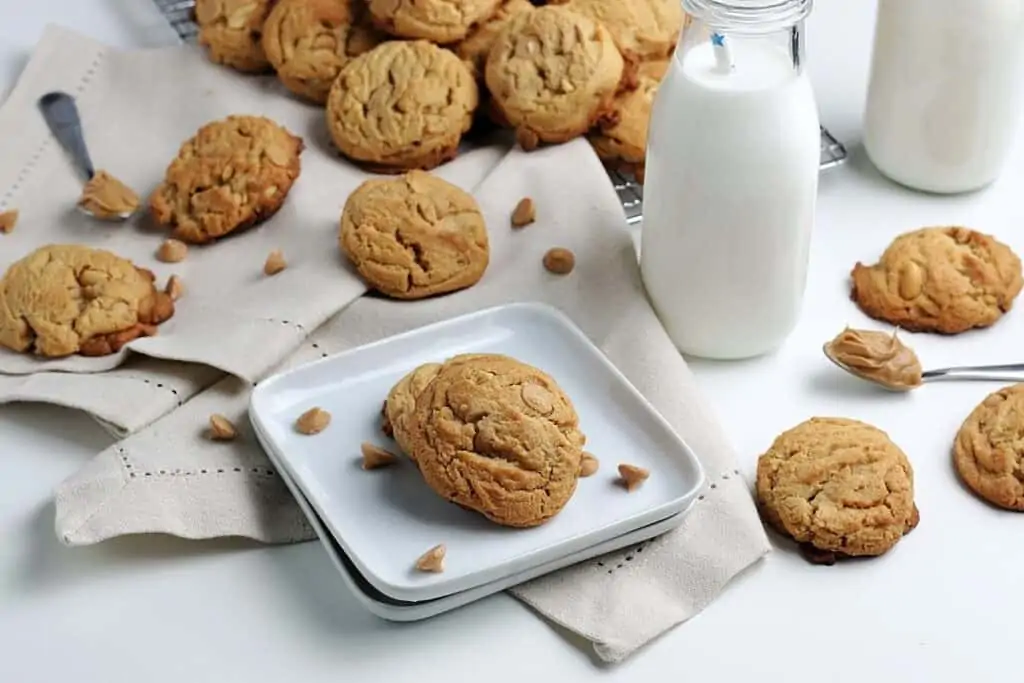 Peanut butter cookies scattered on plates and kitchen clothes with cups full of milk. 