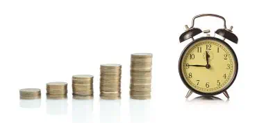 A stack of coins next to a clock.