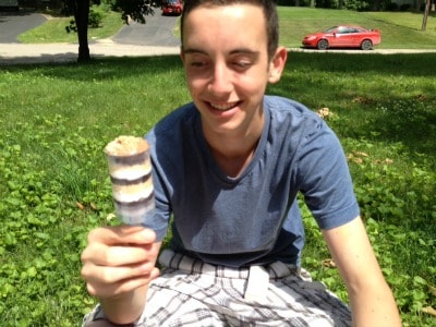 A person sitting in a park eating a smores push pop.