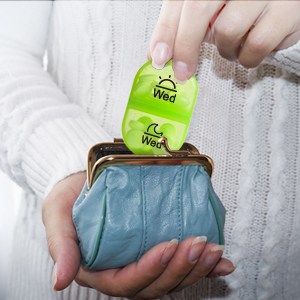A woman pulling out a pill dispenser from a small clutch purse.