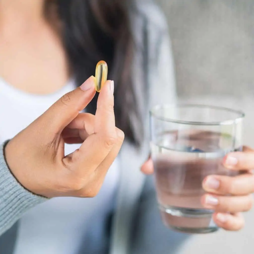 A woman taking a pill with a drink of water.