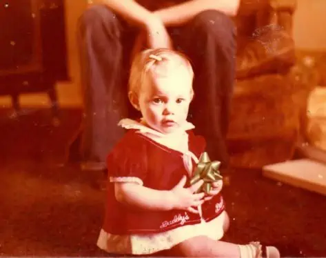 A little girl sitting on the floor while she is holding a Christmas bow.