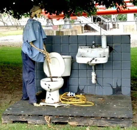 A Halloween decor of a skeleton using a plunger with the toilet in Cedar Point park.