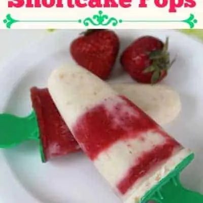 A white plate with strawberry shortcake pops with some strawberries on the side.