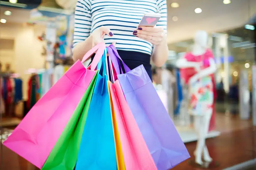 A woman holding several colorful  bags while shopping at the mall.