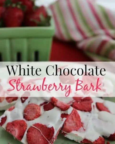 A plate of white chocolate strawberry bark in front of a green basket of fresh strawberries.