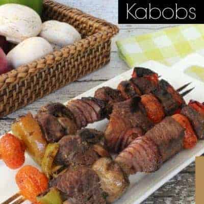 Grilled Steak Kabobs on a white serving tray next to a basket of fresh produce.
