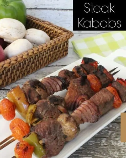 Grilled Steak Kabobs on a white serving tray next to a basket of fresh produce.