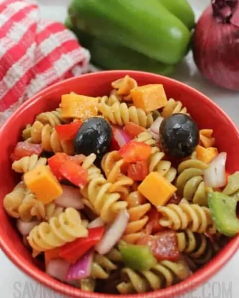 Bowl of cookied pasta salad with cheese cubes, olives, tomatoes, and other garnishings.