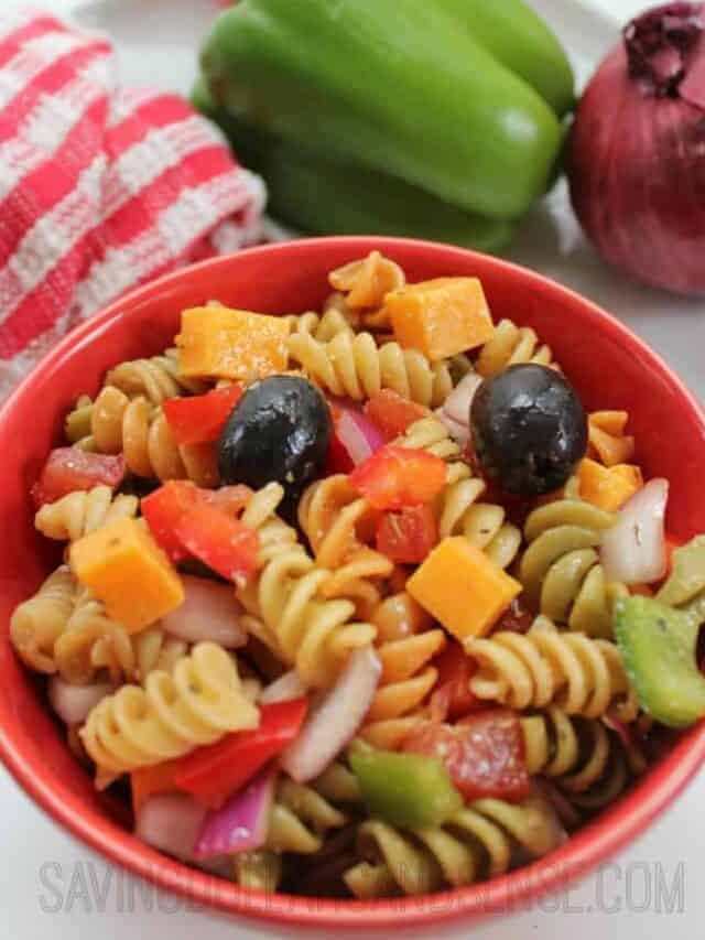 Bowl of cookied pasta salad with cheese cubes, olives, tomatoes, and other garnishings.