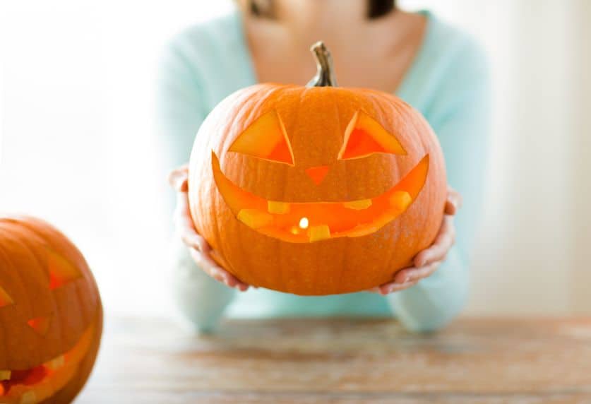 Woman holding a carved pumpkin with a lit candle inside. 
