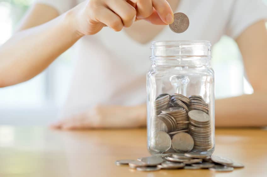 Woman putting coins in a mason jar in order to save money.