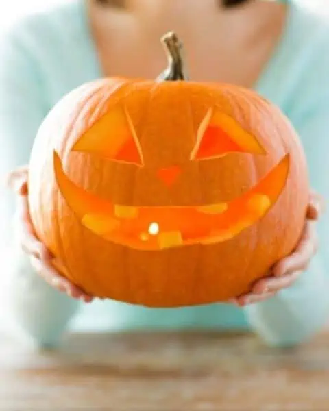 A woman holding a jack-o-lantern with a smile.