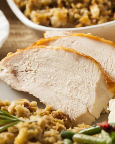 Enjoy a classic Aldi Thanksgiving dinner: sliced turkey breast with stuffing, green beans, mashed potatoes with gravy, and cranberry sauce on a plate. Extra stuffing in a bowl completes this delicious holiday spread.