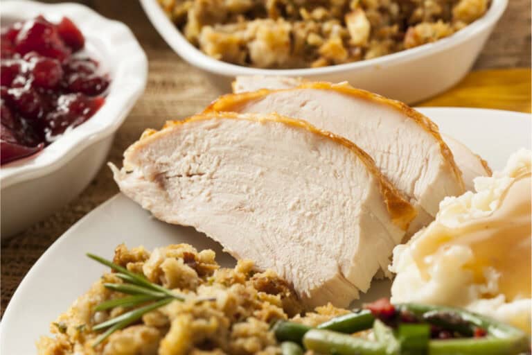 Enjoy a classic Aldi Thanksgiving dinner: sliced turkey breast with stuffing, green beans, mashed potatoes with gravy, and cranberry sauce on a plate. Extra stuffing in a bowl completes this delicious holiday spread.