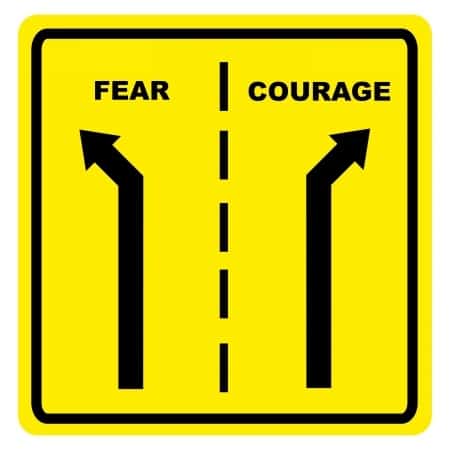 A close up of a sign with two roads that divide between fear and courage.