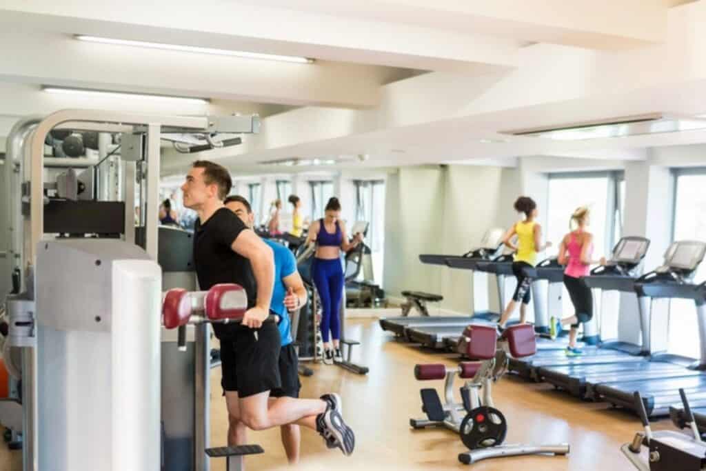 A group of people exercise in a gym, using treadmills, weight machines, and other fitness equipment to stay fit and cut gym costs through shared memberships.