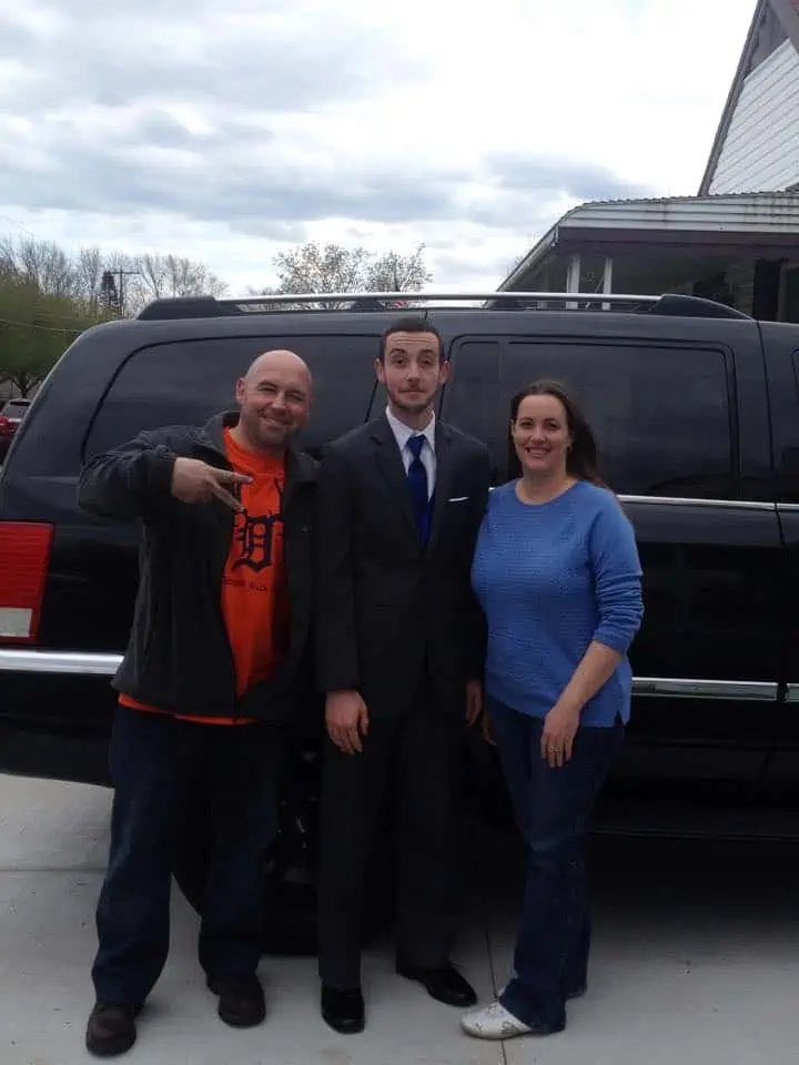 Parents with their young adult son who is dressed up in a suit and tie.