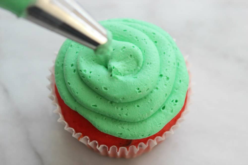 Piping green frosting on a cupcake.