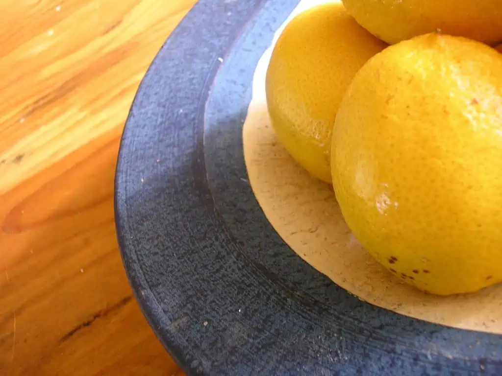 A bowl of oranges sitting on top of a wooden table, with Lemon and Fruit