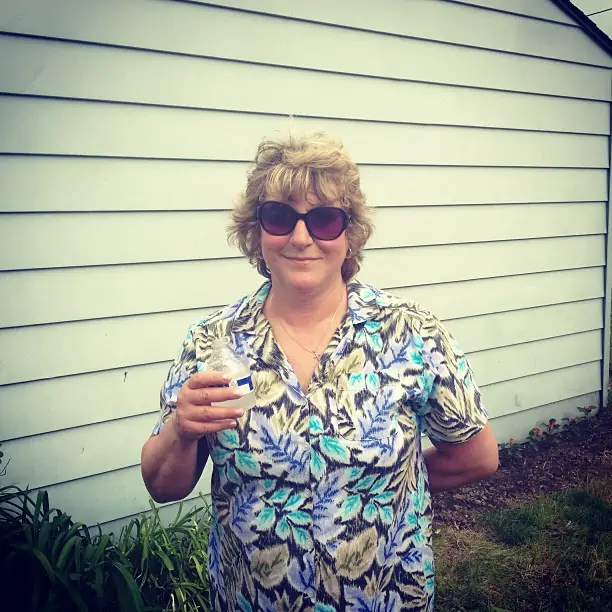 A woman wearing sunglasses standing outside of a home.