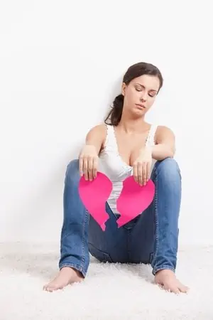 A woman sitting on the ground with a paper heart ripped in half. 
