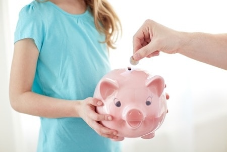 A parent filling up a child\'s piggy bank. How to teach kids financial responsibility.