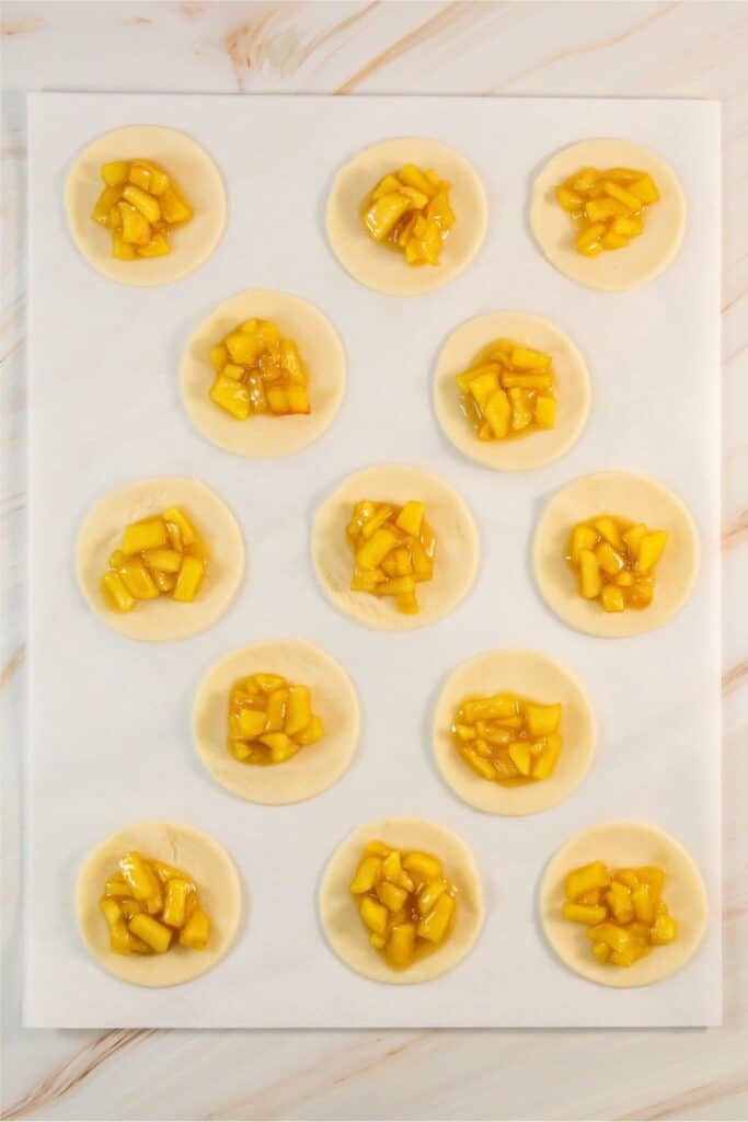 A baking sheet with 15 round raw dough pieces topped with diced mango filling, arranged in rows on a white background, reminiscent of an Apple Pie Cookie Recipe.