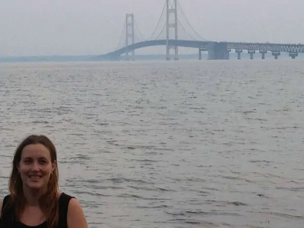 A woman standing next to a body of water and the Golden Gate bridge.