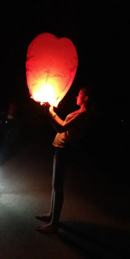 A person standing with a lit up lantern in the dark.