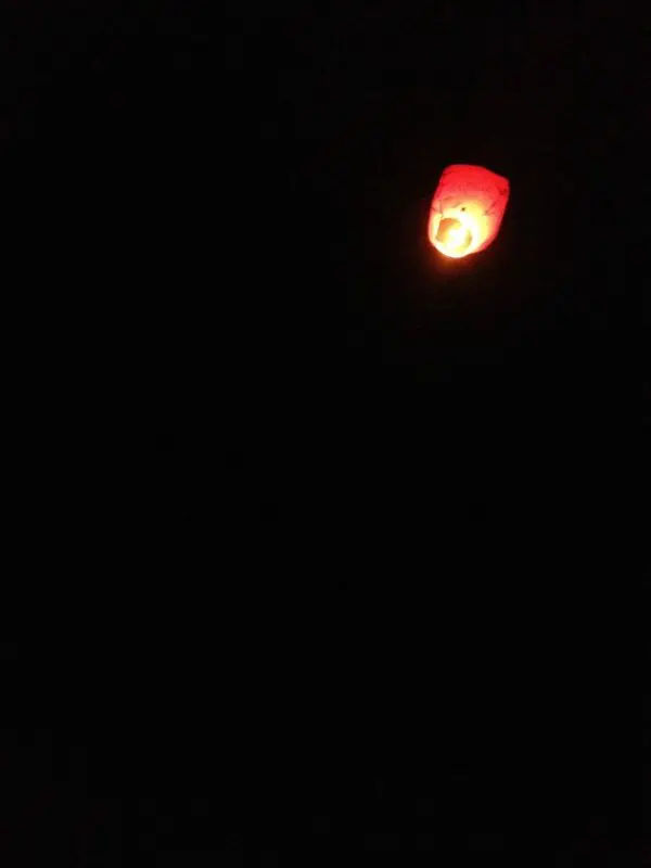 A close up of a lit lantern floating away in the sky.