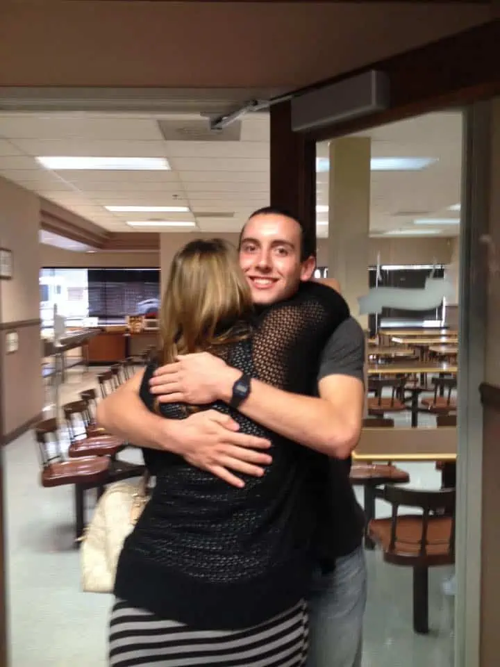 A mom hugging her grown son in a public room.