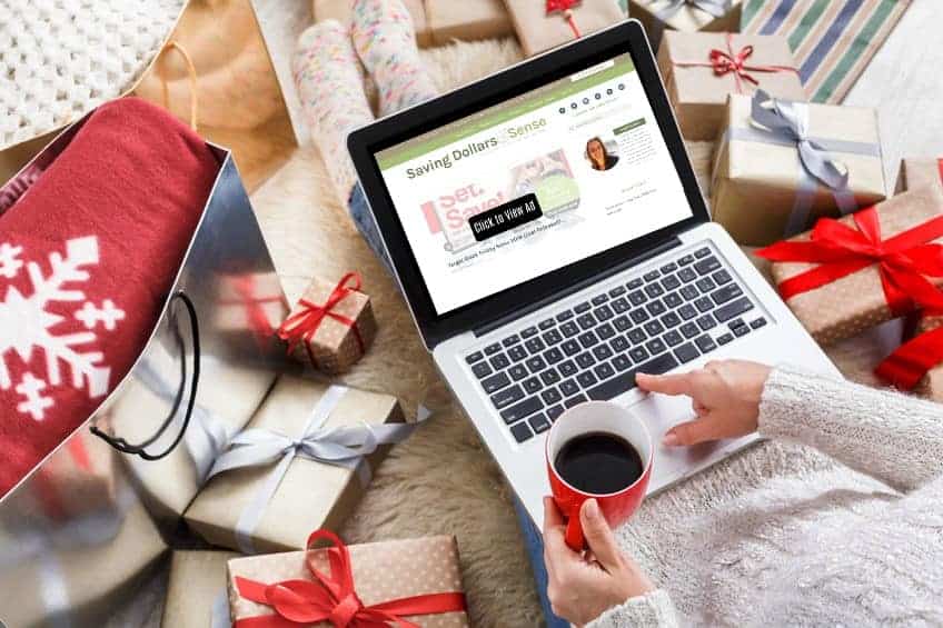 A laptop computer sitting on top of a bed. Woman is surrounded by Christmas presents and a cup of coffee.