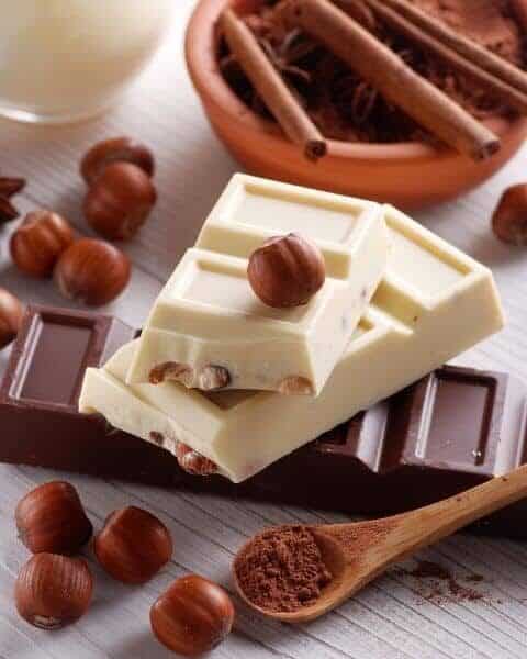 Milk and white chocolate stacked on top of each other with cinnamon sticks, and nuts.