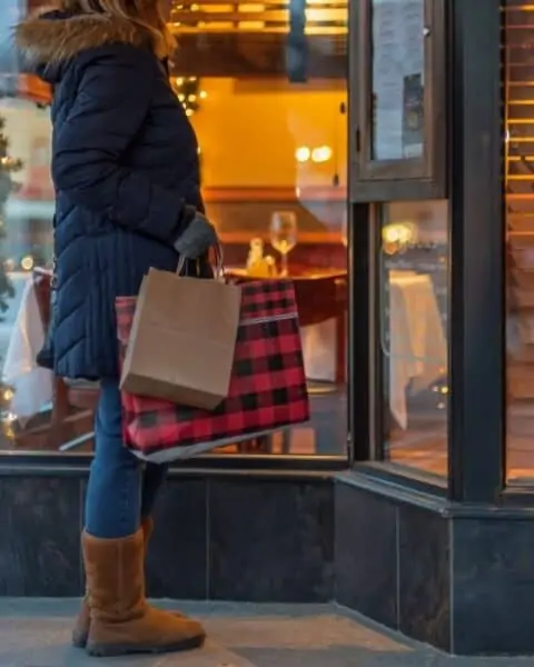 A woman dressed in winter clothes stands in front of a store while shopping for Christmas gifts.