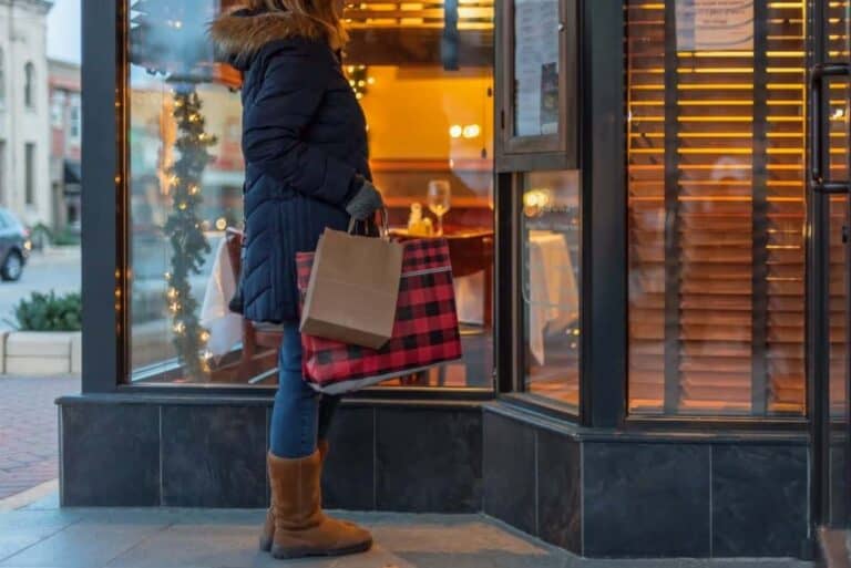 A woman dressed in winter clothes stands in front of a store while shopping for Christmas gifts.