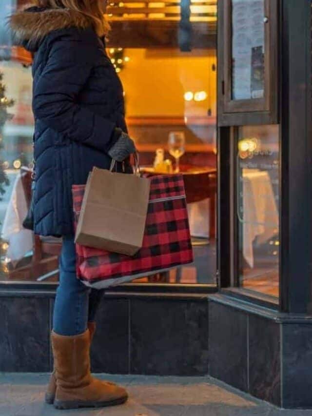 A woman dressed in winter clothes stands in front of a store while shopping for Christmas gifts.
