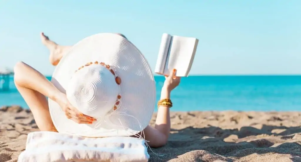 Woman laying on the beach reading a book.