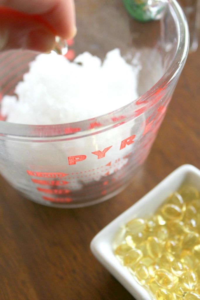 A person adding Vitamin E capsules to a measuring bowl of coconut oil. 