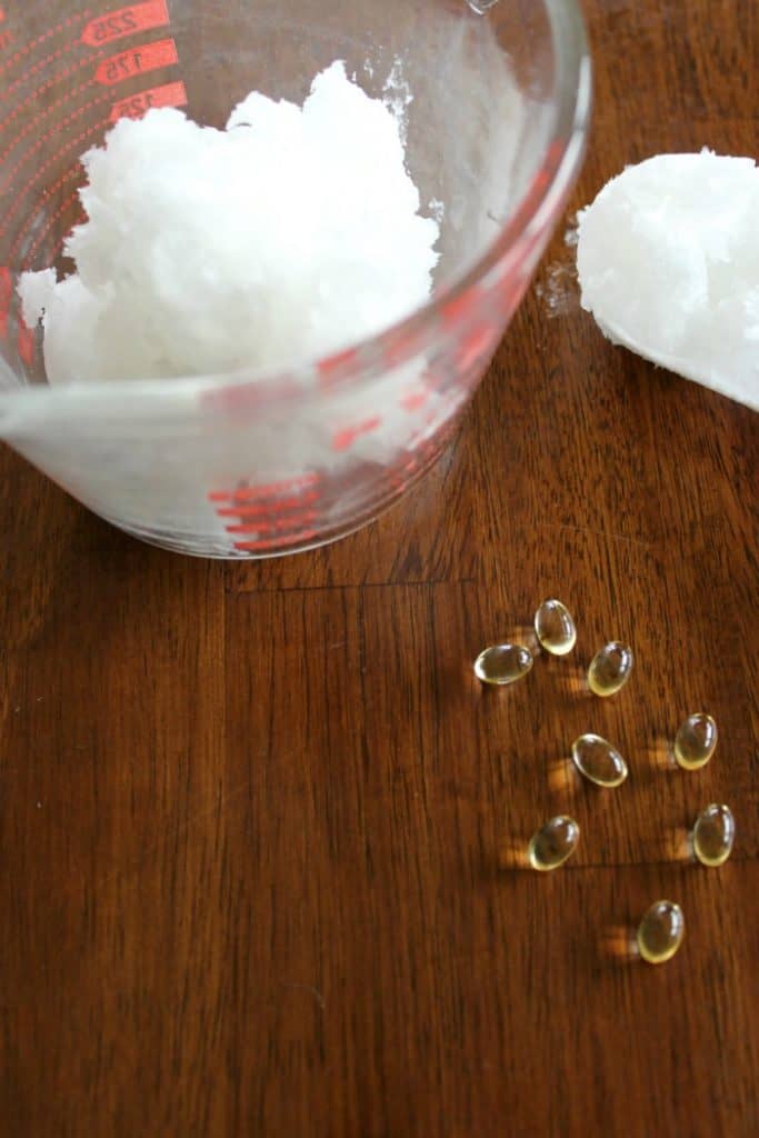 Coconut oil in a glass measuring bowl with some vitamin E capsules on the table. 