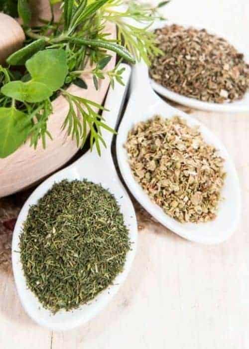 Three white seasoning spoons with dried herbs.