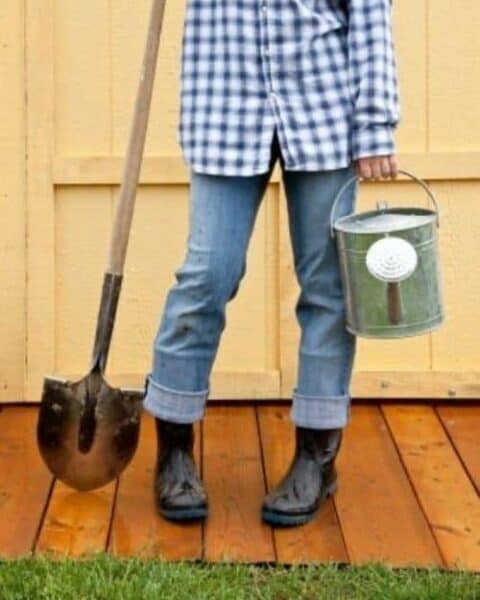 A woman holding a watering pail and shovel.
