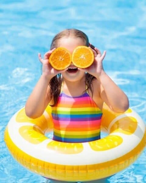 A little girl in a swimming suite playing in a pool.