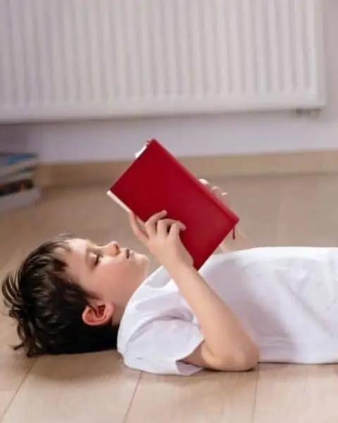 A young boy laying on his back, reading a chapter book.