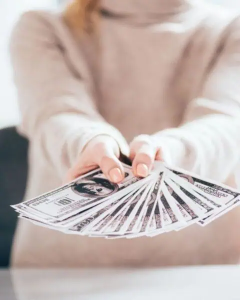 In a bright room, someone proudly displays a fan of U.S. hundred-dollar bills on the table, showcasing the potential to make money selling stuff.