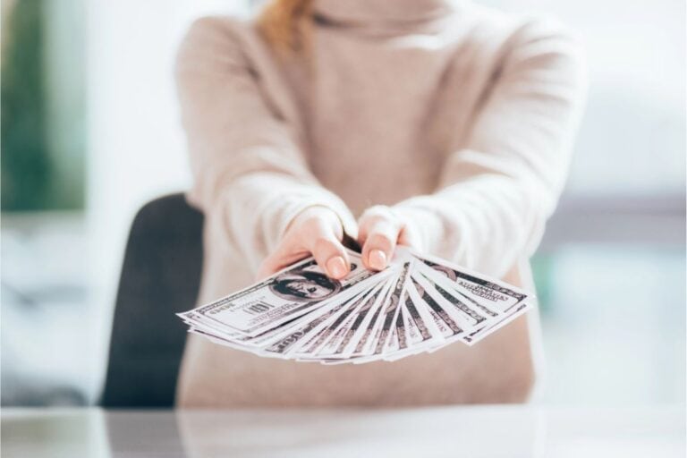 In a bright room, someone proudly displays a fan of U.S. hundred-dollar bills on the table, showcasing the potential to make money selling stuff.