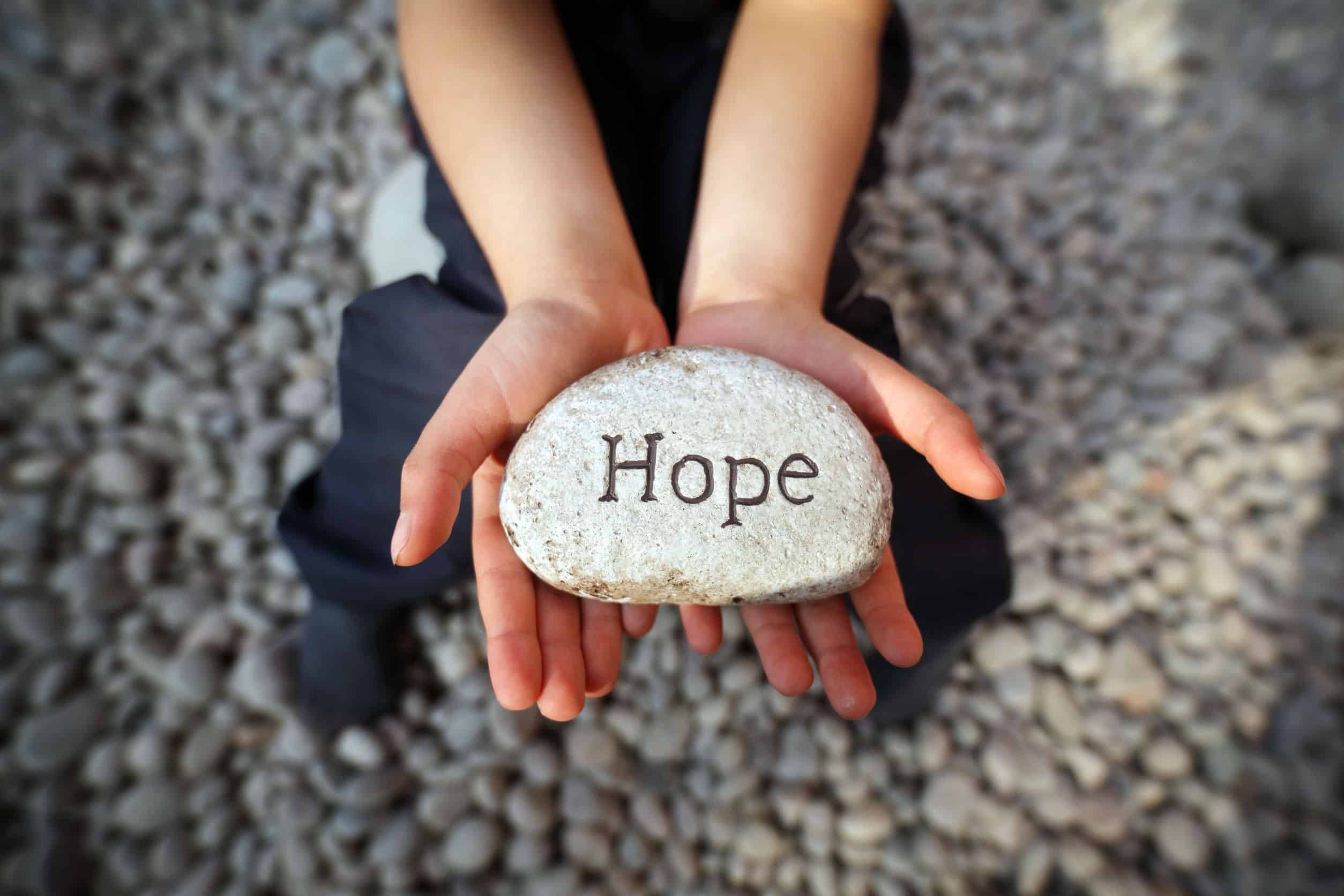 A girl holding a rock with the word inscribed that reads, \"hope.\"