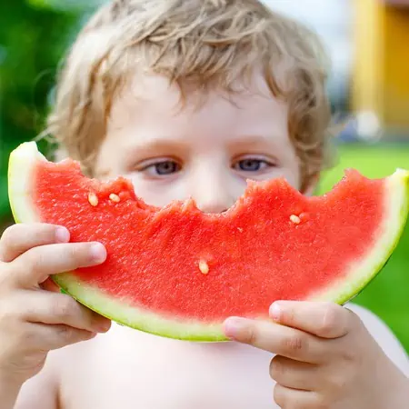 A close up of a kid holding a slice of partially eaten watermelon. 